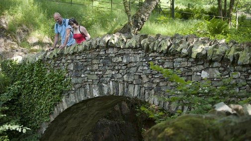 Two people viewing the waterfall from a stone bridge at Aira Force